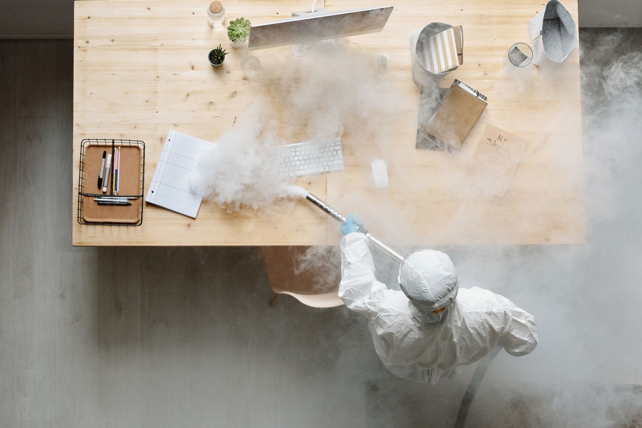 Une personne désinfecte un espace de travail par fumigation, en portant un équipement de protection complet pour garantir sa sécurité.